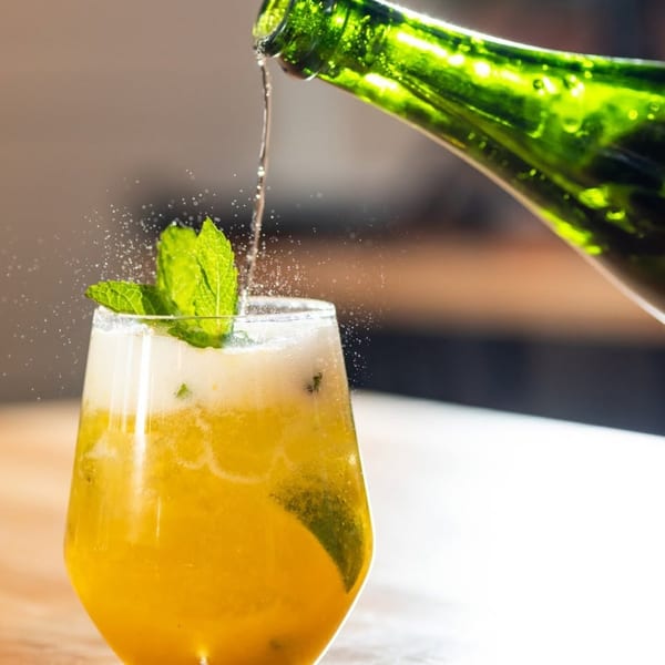 Sparkling beverage poured from a green bottle into a glass with mint and citrus.