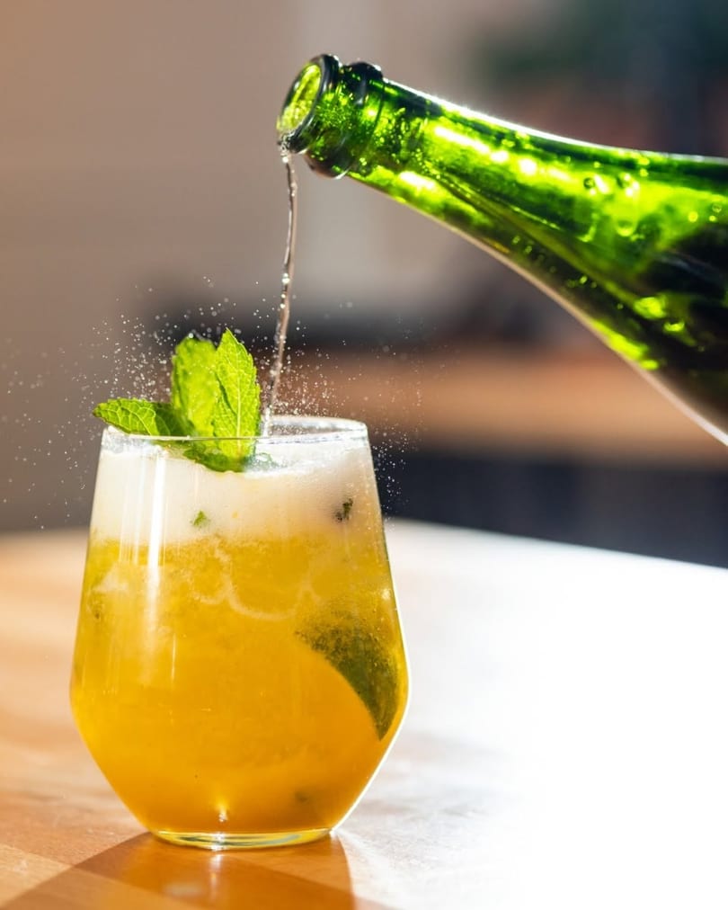 Sparkling beverage poured from a green bottle into a glass with mint and citrus.